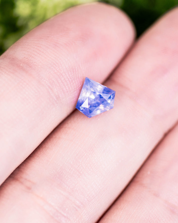 1.28 carat opalescent white and cornflower blue parti sapphire resting on fingertip, showing mixed hues and precision shield modified brilliant cut, untreated gemstone from Sakaraha, Madagascar.