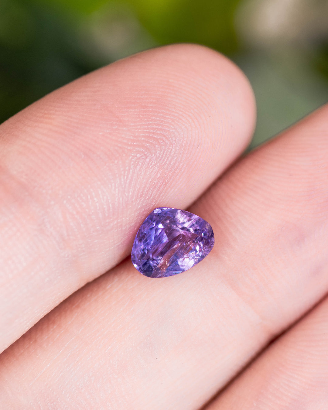 1.29 carat violet lavender sapphire resting on fingertip, revealing delicate brilliance and pastel tones in a trilliant modified brilliant cut, untreated gemstone from Umba River, Tanzania.