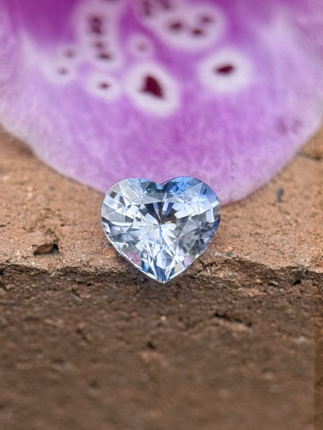 1.30ct custom brilliant heart cut sapphire with striking blue and colorless parti zoning, resting on a soft neutral stone surface – sourced from Sakaraha, Madagascar.