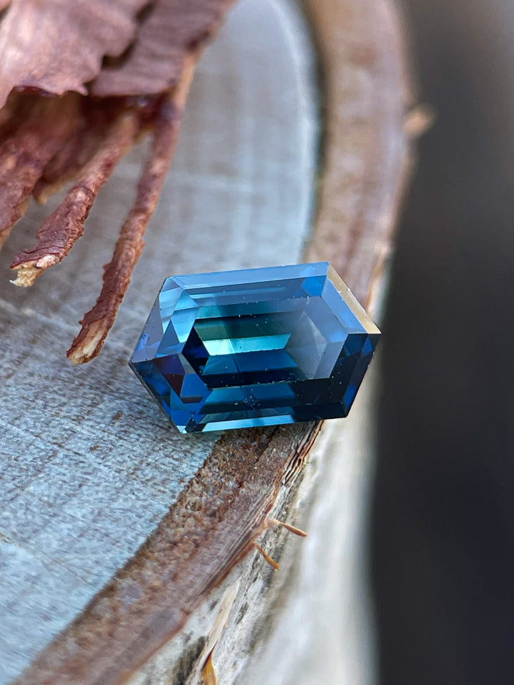 A natural teal-blue Nigerian sapphire resting on a textured surface, displaying its mesmerizing step-cut facets.