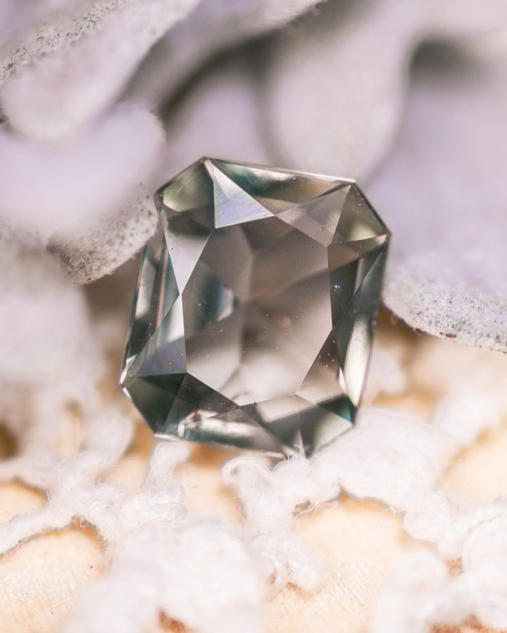 1.31 carat teal, yellow, and green sapphire resting on soft white fabric, displaying brilliance and clarity in a custom modified radiant cut, untreated gemstone from Umba River Valley, Tanga, Tanzania.