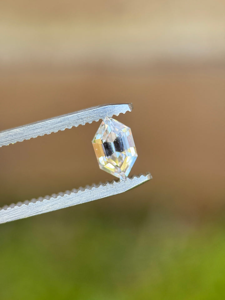 1.31 carat pale yellow gray sapphire hexagon step cut held in tweezers showing crisp geometric facets, loose gemstone.