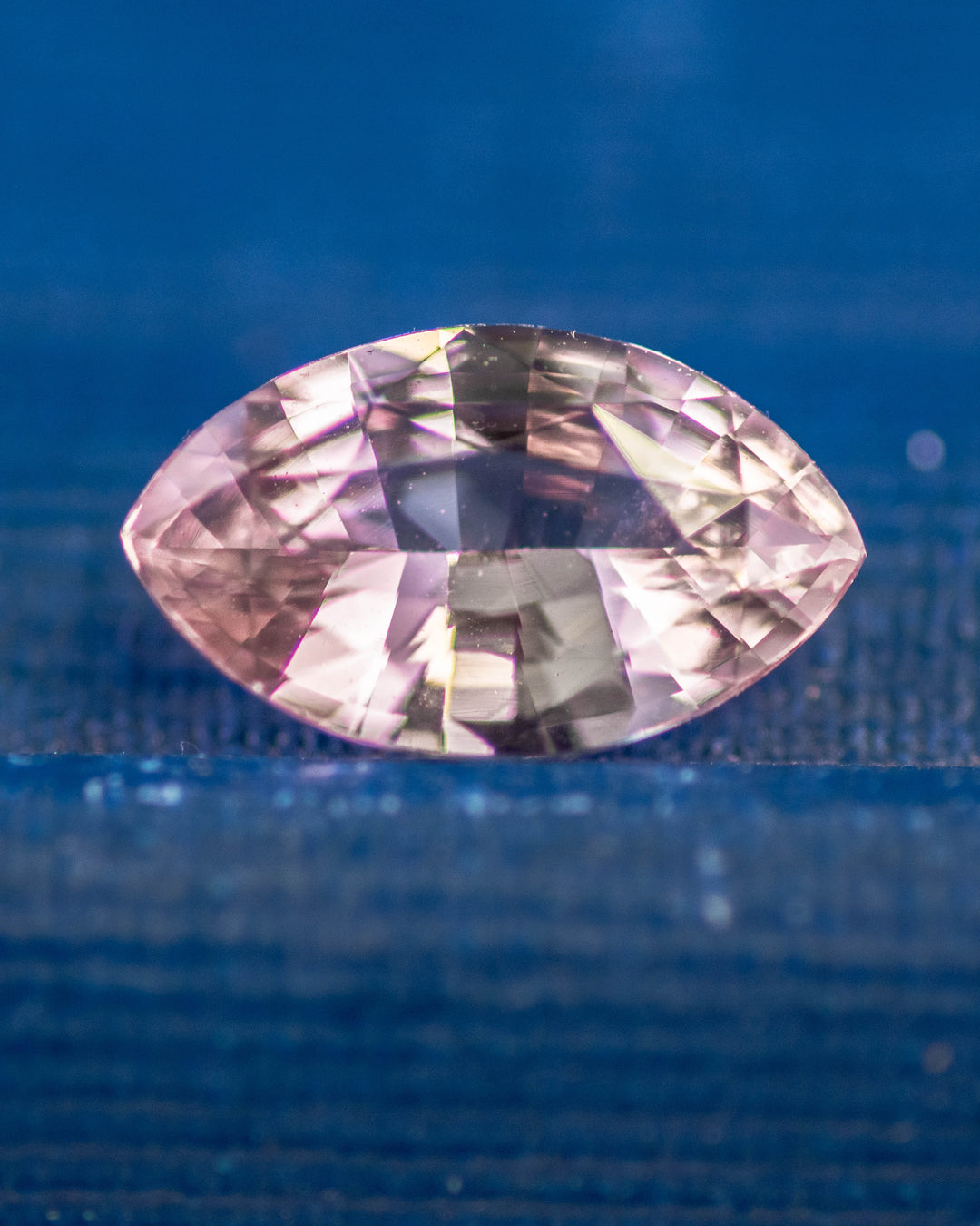 1.32 carat salmon pink and peach sapphire resting on a deep blue surface, showing vibrant pastel hues and reflective brilliance in a precision marquise mixed cut, untreated sapphire from Sakaraha, Madagascar.