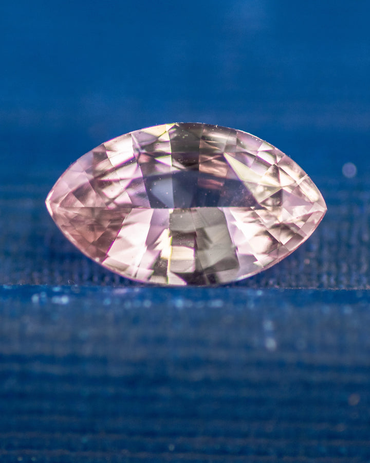 1.32 carat salmon pink and peach sapphire resting on a deep blue surface, showing vibrant pastel hues and reflective brilliance in a precision marquise mixed cut, untreated sapphire from Sakaraha, Madagascar.