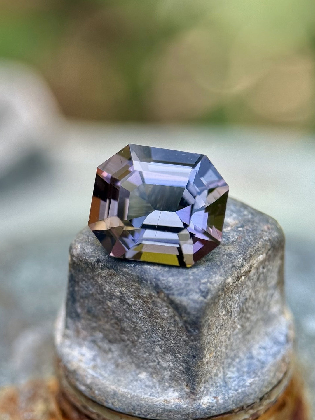 Emerald cut Tanzanite weighing 1.32CT with teal and violet mermaid color blend, styled outdoors on a textured surface.