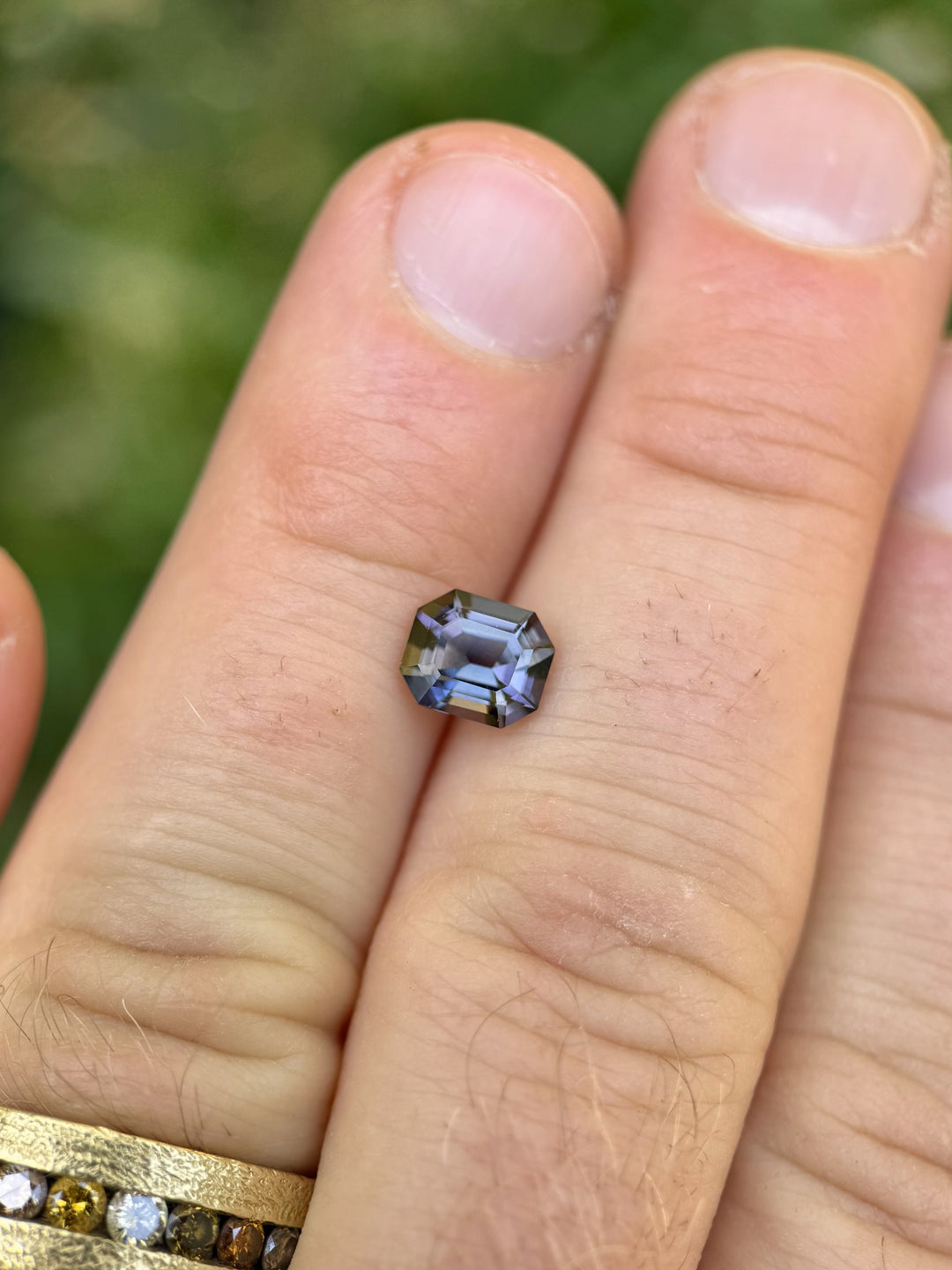 Merelani Hills Tanzanite in emerald cut with teal and purple hues, resting on fingers to show scale and clarity.