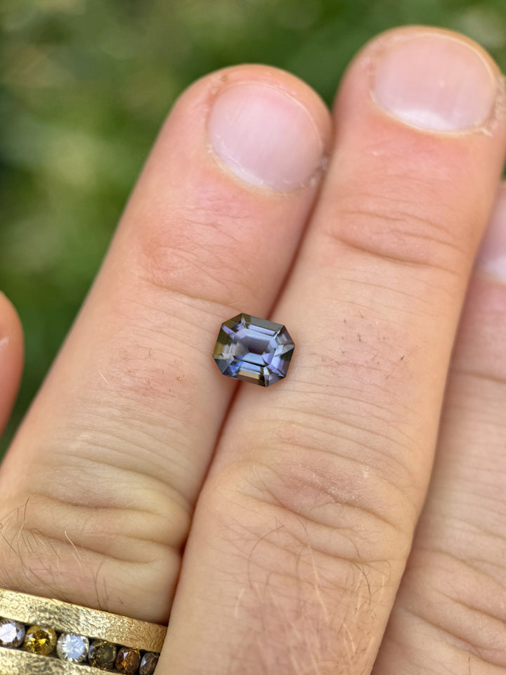 Merelani Hills Tanzanite in emerald cut with teal and purple hues, resting on fingers to show scale and clarity.