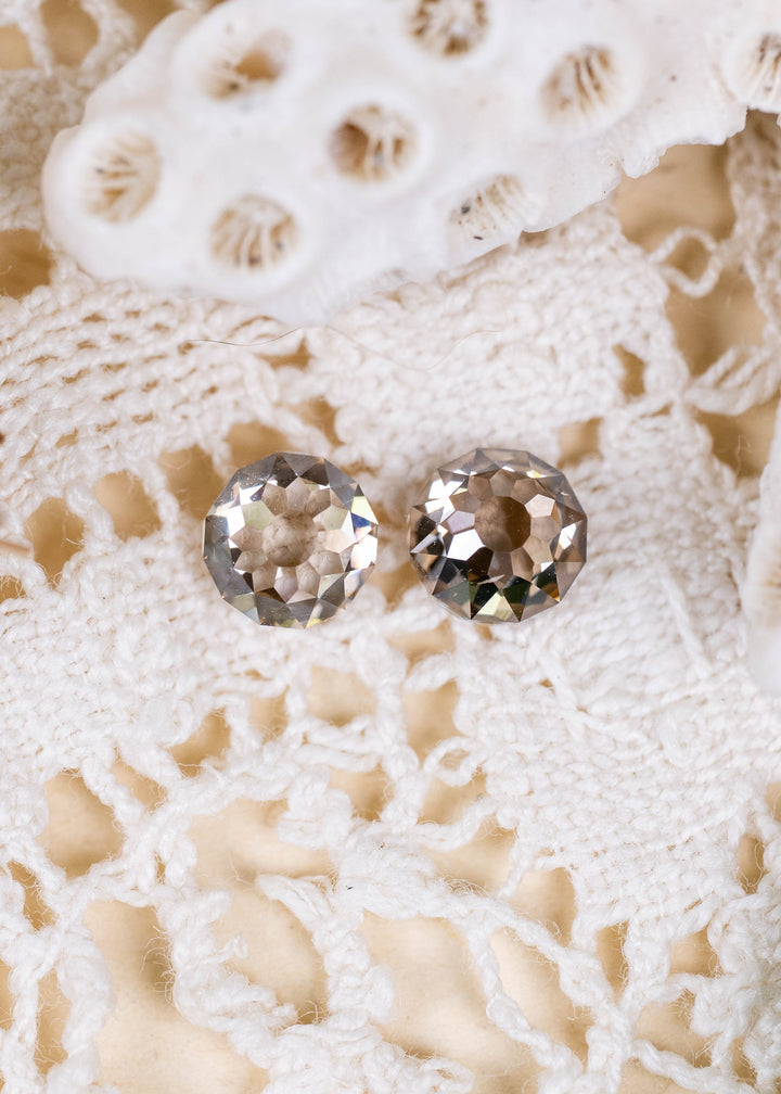 A pair of South African Round Mughal cut diamonds weighing 1.32 carats total, photographed on ivory lace. Their contrasting C1–C3 champagne tones, VVS2 clarity, and distinctive geometric faceting create an elegant antique-inspired appearance.