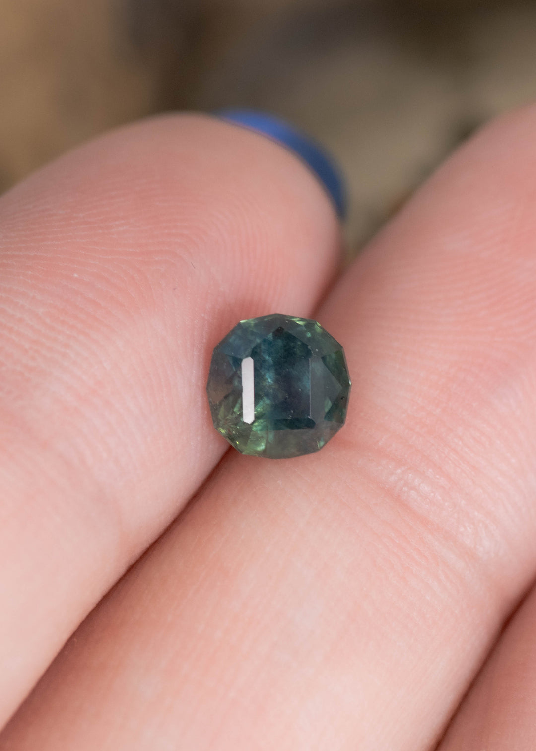 1.32 carat unheated Montana sapphire resting on fingers for scale, blue green teal geometric rounded cushion cut from El Dorado Bar Deposit with natural brilliance