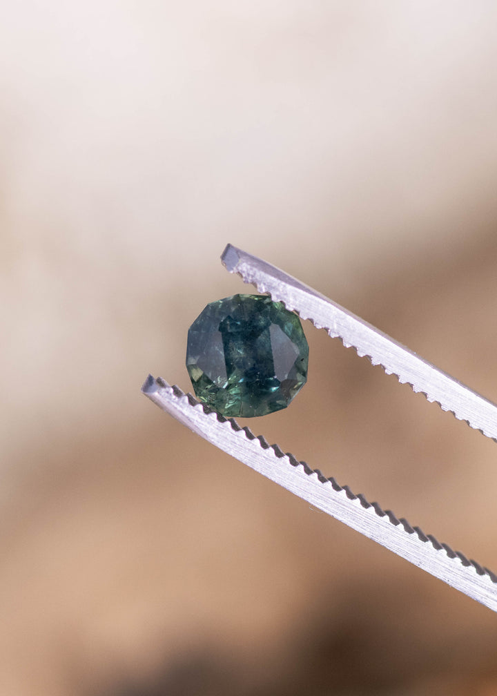 1.32ct blue green teal Montana sapphire held in tweezers, geometric rounded cushion cut showing precision faceting and natural color zoning from El Dorado Bar