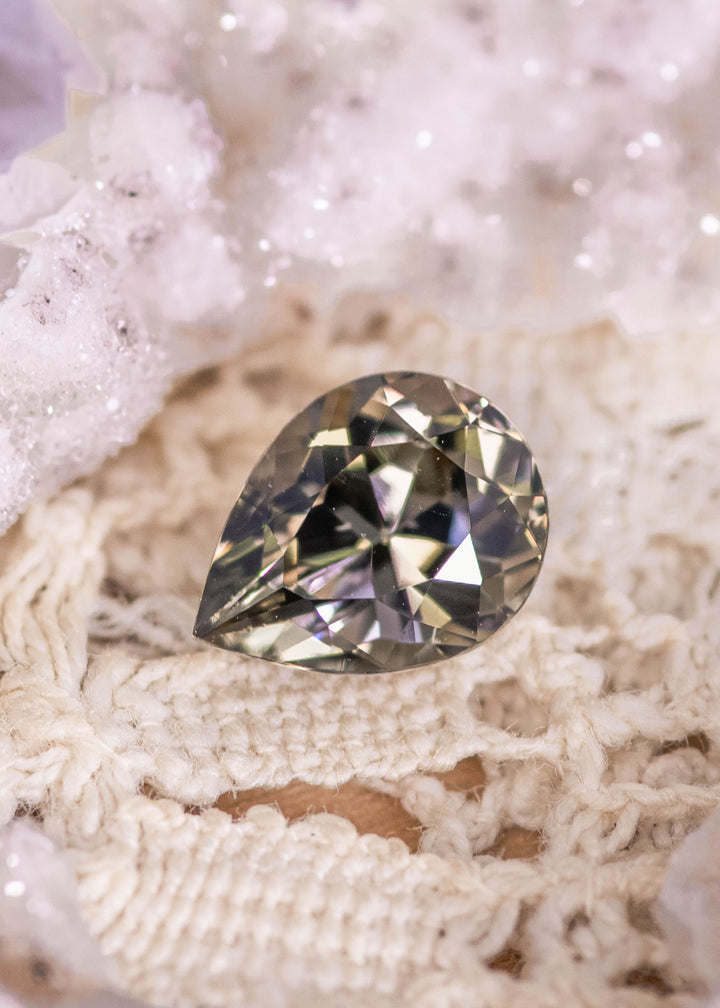Natural 1.32 carat Tanzanite pear brilliant on crocheted fabric showing trichroic green brown purple hues and clean faceting from Tanzania