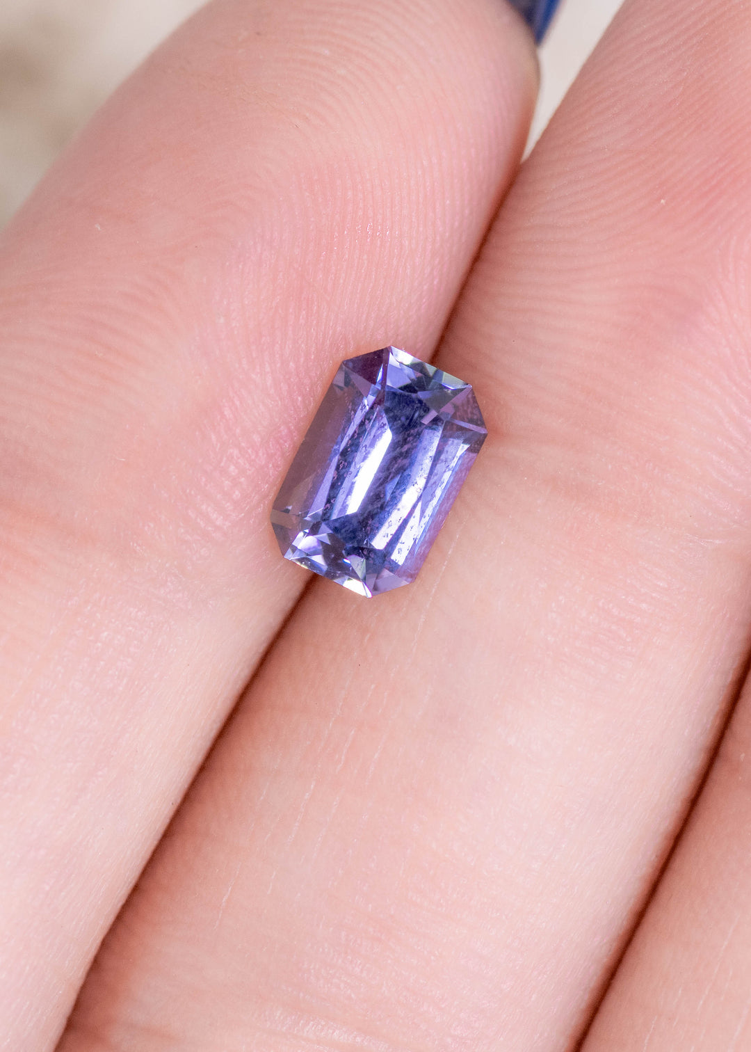 Loose mermaid-toned tanzanite resting on fingers, showing the shifting purple, blue, and green hues within the modified radiant cut.