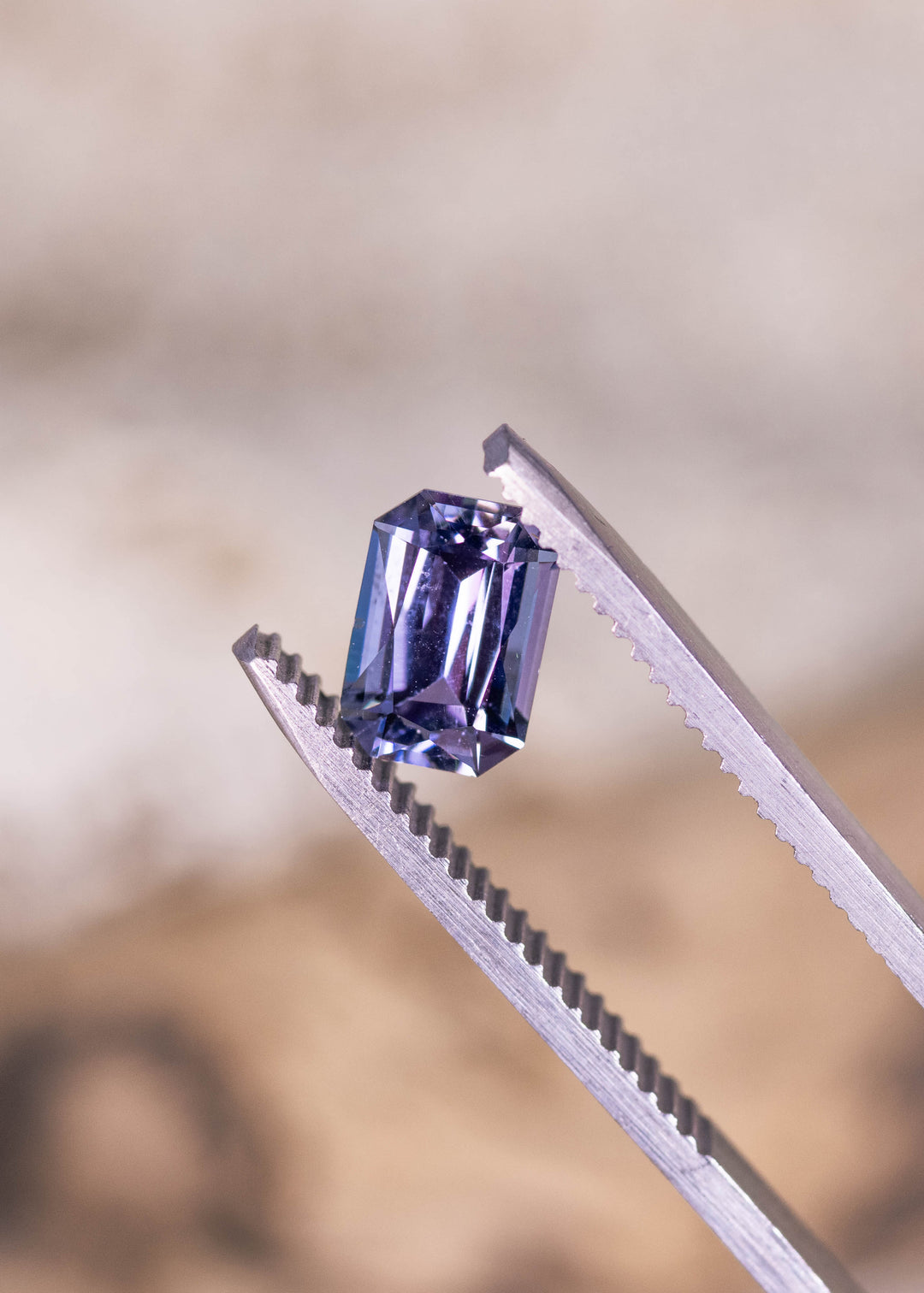 Loose purple, blue, and green tanzanite held in tweezers, highlighting the crisp facet pattern of the custom modified radiant cut from Tanzania.