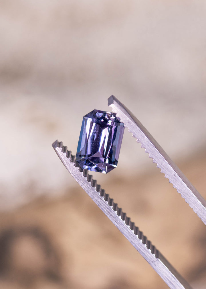 Loose purple, blue, and green tanzanite held in tweezers, highlighting the crisp facet pattern of the custom modified radiant cut from Tanzania.