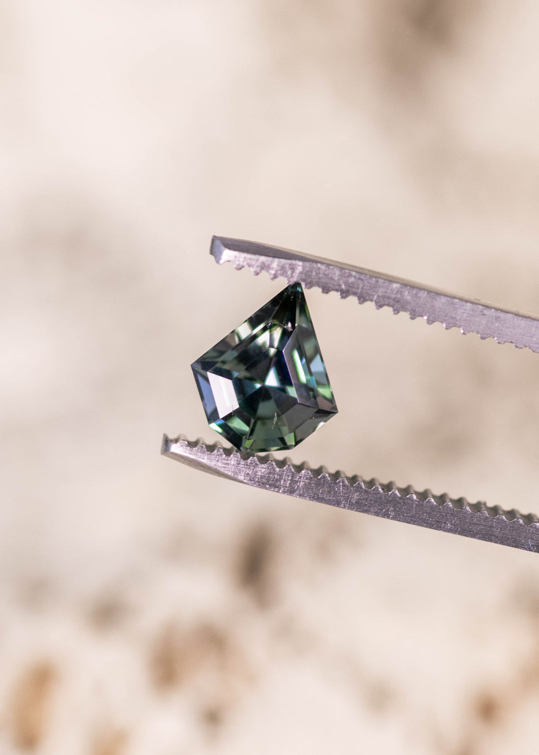 1.36 carat yellow green teal Tanzanite geometric mix cut shield held in tweezers, untreated Merelani Hills Arusha Tanzania gemstone displaying crisp facet reflections, color shift and designer shape for fine jewelry design
