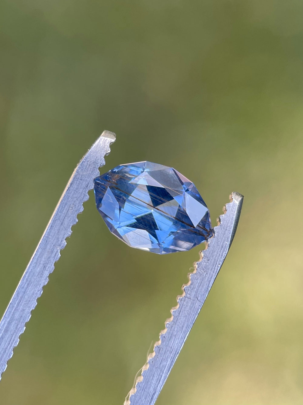 1.36 carat untreated sapphire in a custom geometric marquise cut showing a rich blue and periwinkle color, photographed against fingers for scale.
