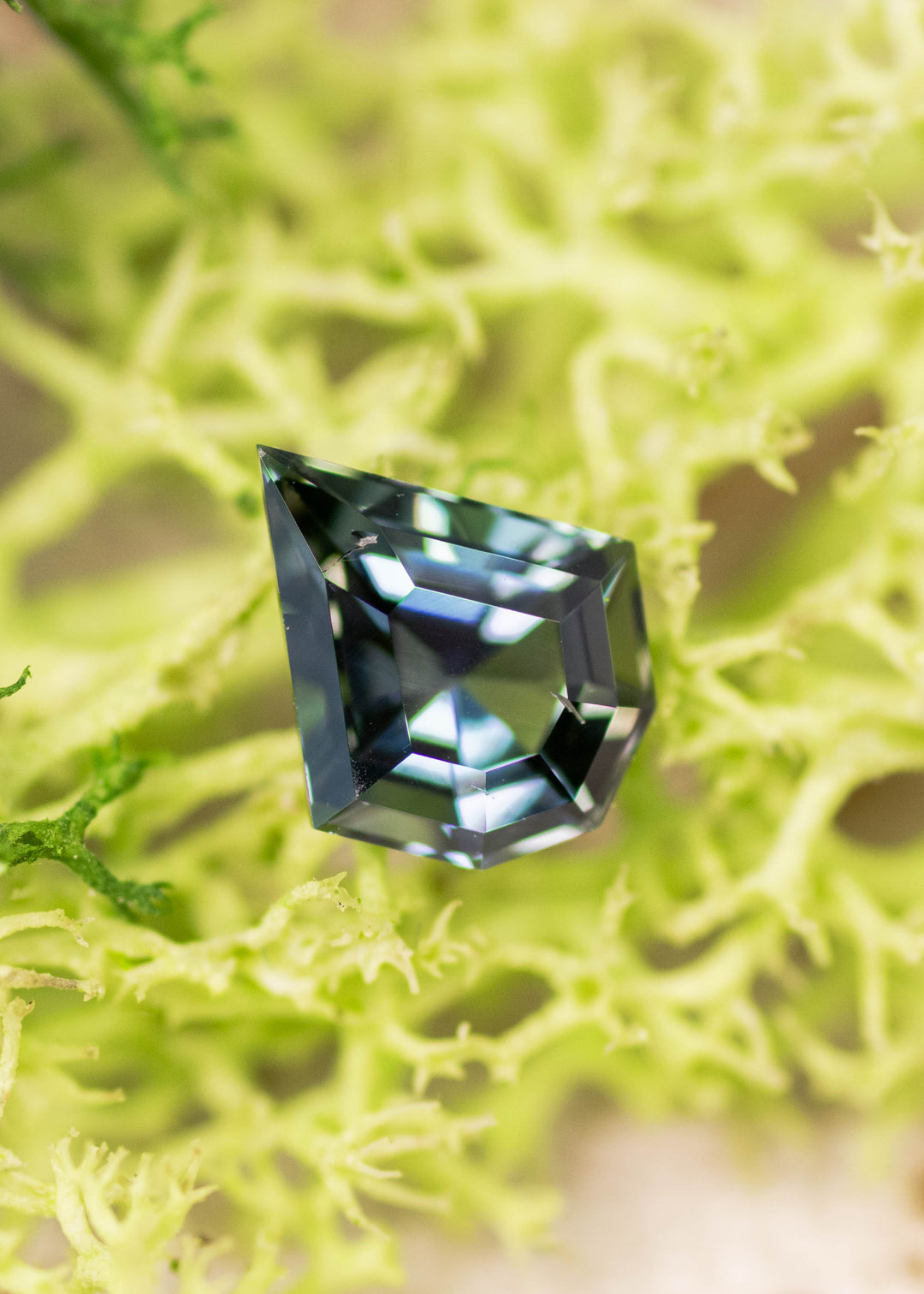 1.36 carat yellow green teal Tanzanite custom geometric mix cut shield displayed on natural surface, untreated gemstone from Merelani Hills Tanzania showing precision faceting, sharp angles and multicolor brilliance for custom jewelry