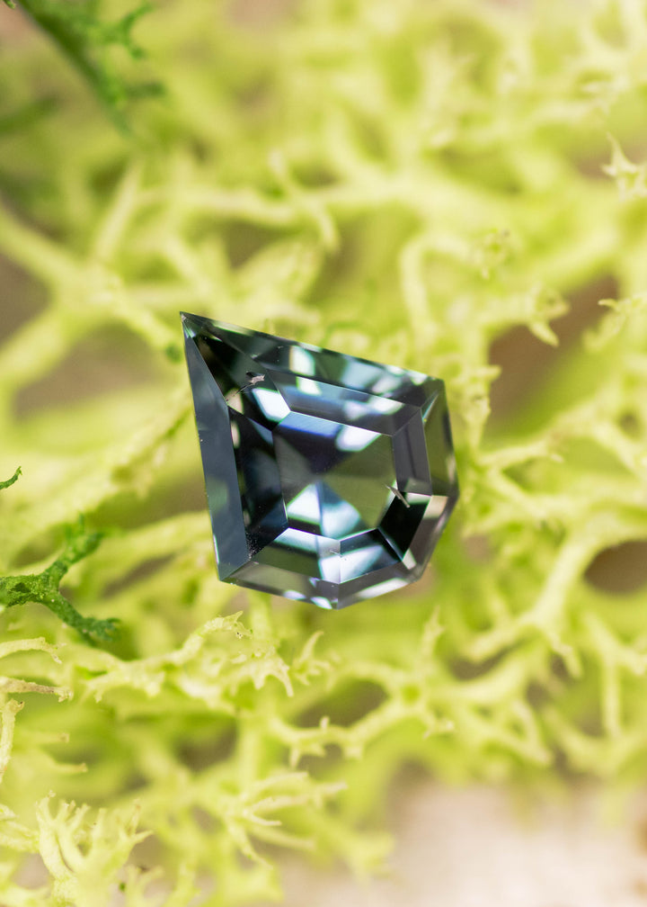 1.36 carat yellow green teal Tanzanite custom geometric mix cut shield displayed on natural surface, untreated gemstone from Merelani Hills Tanzania showing precision faceting, sharp angles and multicolor brilliance for custom jewelry