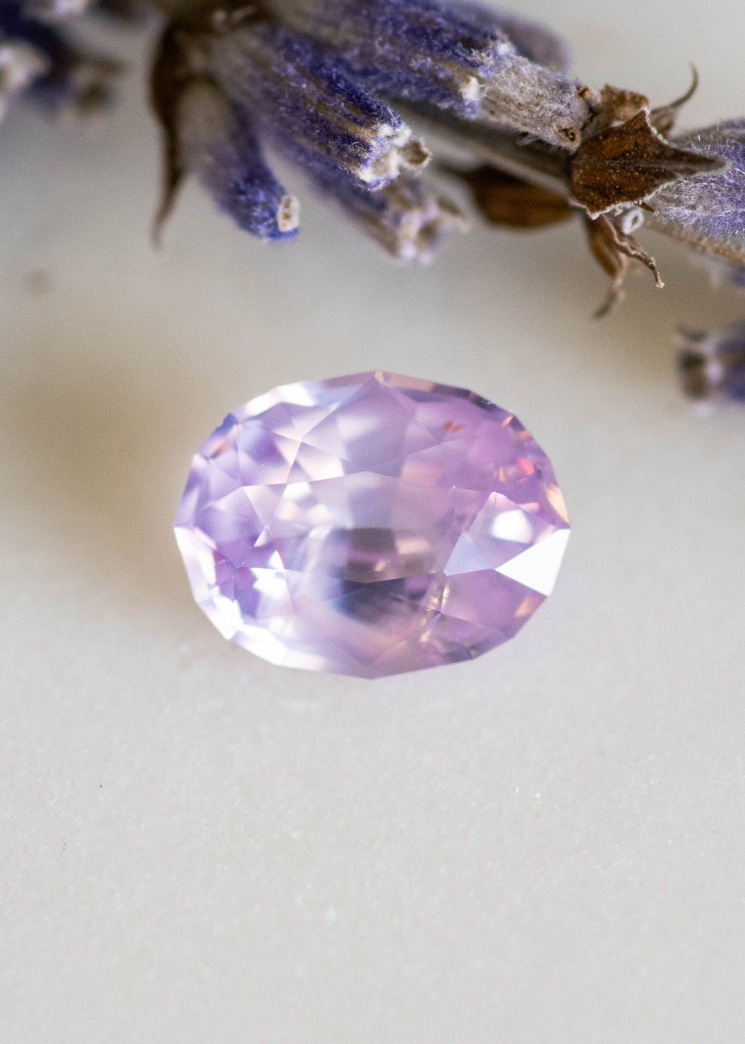 Loose 1.37 carat opalescent pink peach sapphire from Ratnapura shown face-up on a white surface, displaying soft pastel glow and precision oval mix cut facets.