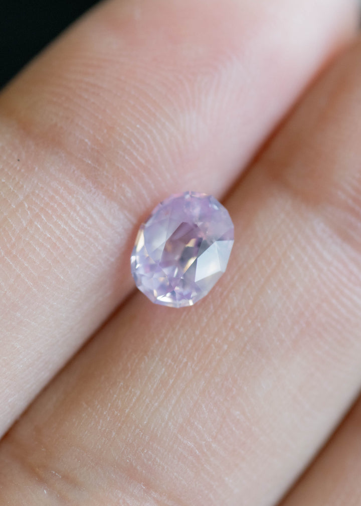 Loose 1.37 carat pink peach sapphire resting on fingertips, highlighting the oval mix cut symmetry and soft opalescent sheen.