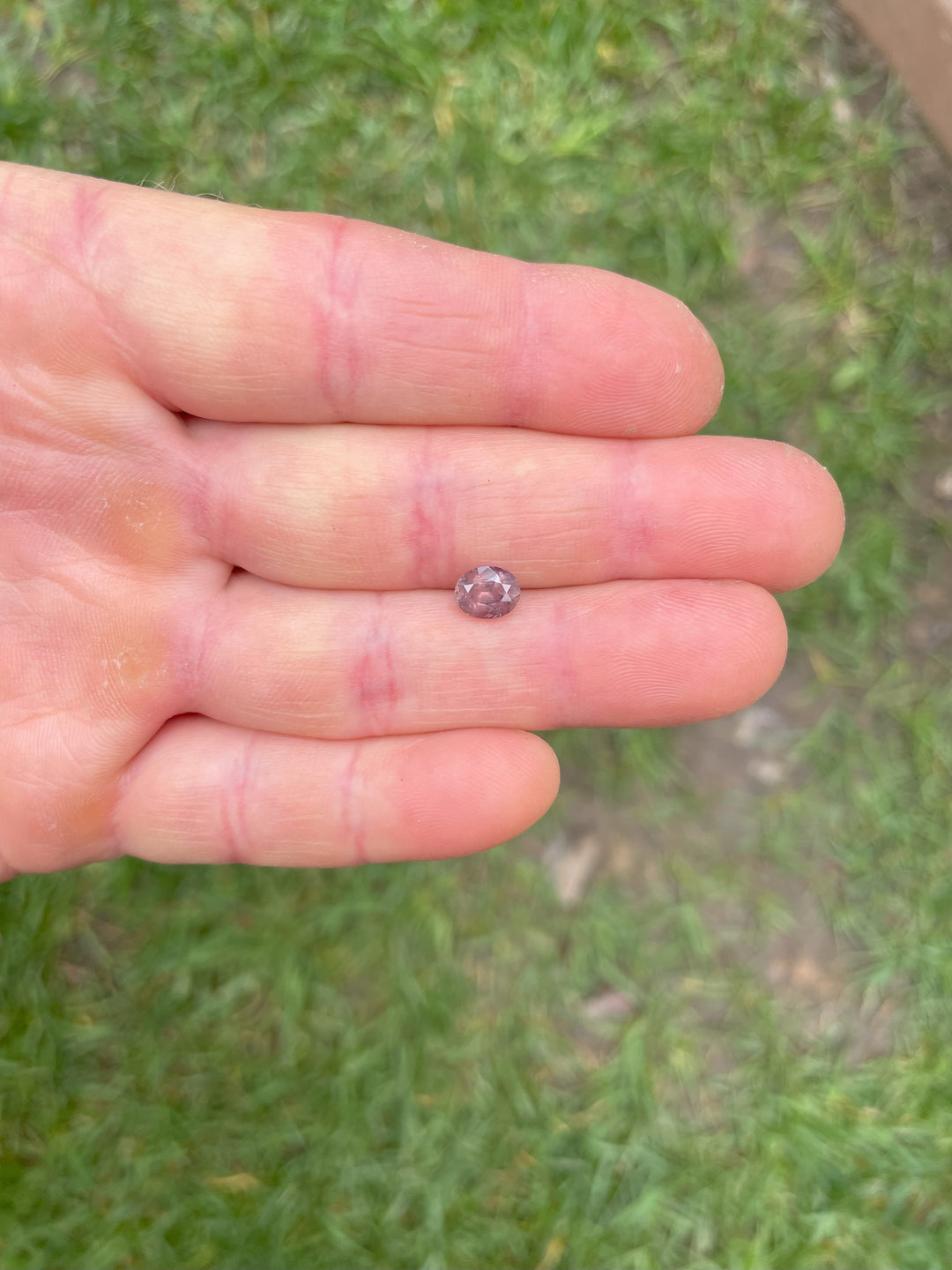 Handshot of 1.37ct color-shifting sapphire in peach pink mauve hues, oval cut, from Umba River, Tanzania