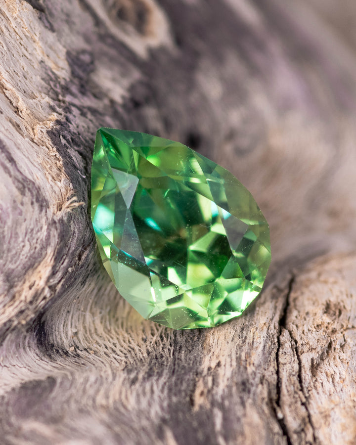 1.39 carat electric lime green tsavorite garnet resting on natural wood texture, showcasing its vivid brilliance and clarity in a pear cut, untreated gemstone from Kenya.