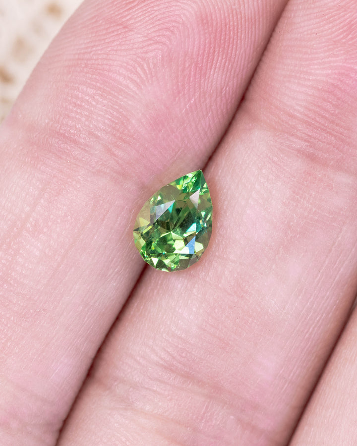 Close-up of 1.39 carat tsavorite garnet resting on fingertips, revealing rich electric green hues and brilliant reflections in the pear cut, untreated gemstone from Kenya.