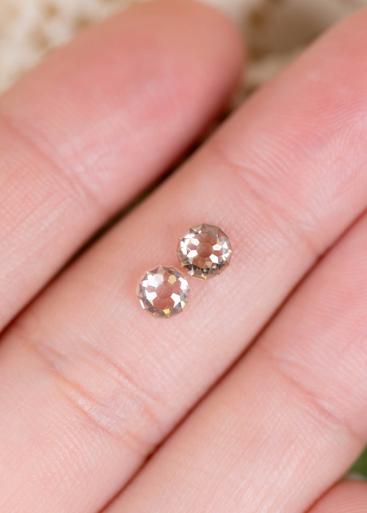 A 1.39ct total weight pair of South African Round Mughal cut diamonds photographed on fingers for scale. Their pale champagne tones and unusual faceting make them appealing for bespoke diamond earrings and heirloom jewelry.