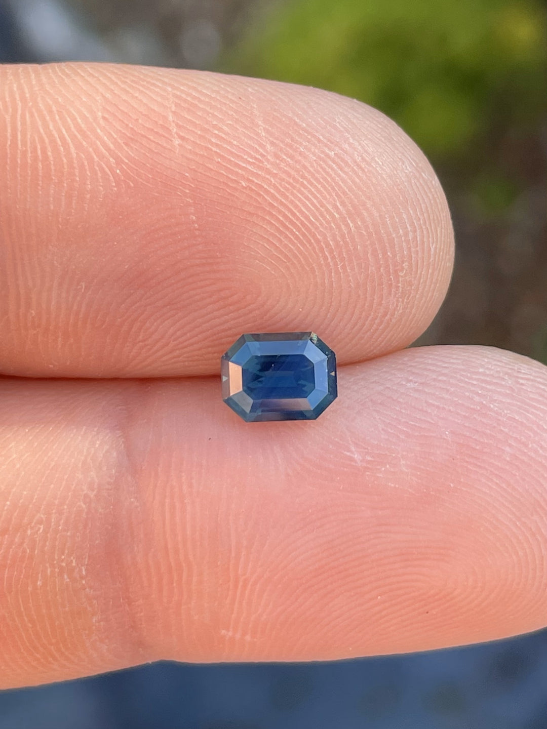 A 1.40-carat teal sapphire with an octagonal step cut, delicately placed on a fingertip, showcasing its deep blue-green hues. Ethically sourced from Gombe, Nigeria.