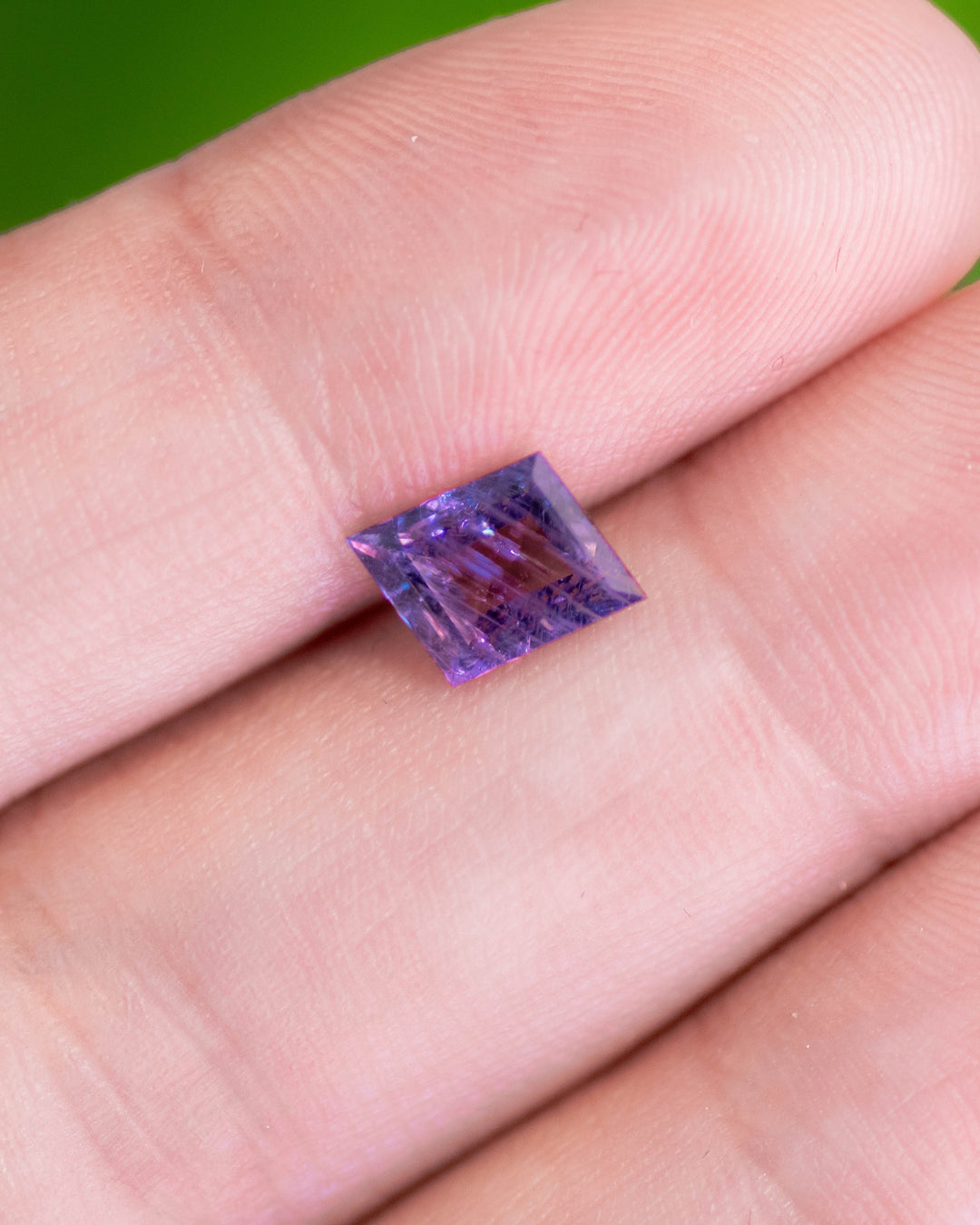 1.40 carat purple sapphire displayed on fingertips under natural light, revealing sharp facet reflections, rhombus step cut geometry, and the rich violet tone of this untreated sapphire from Tanzania.