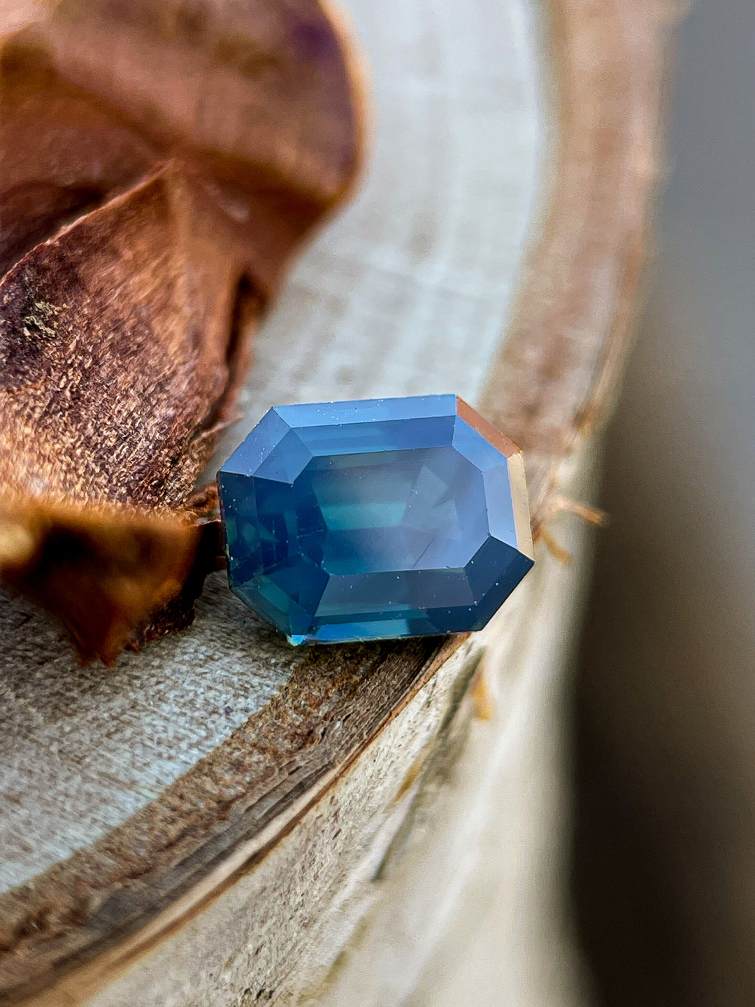 A natural Nigerian sapphire with deep green and blue tones, resting on a wooden surface, displaying its mesmerizing transparency.