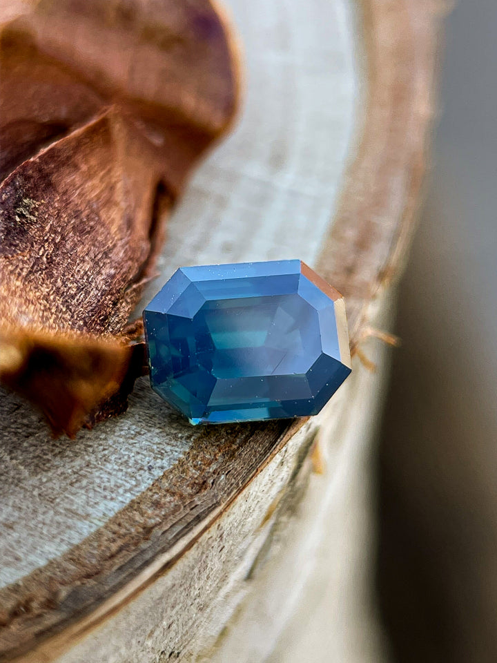 A natural Nigerian sapphire with deep green and blue tones, resting on a wooden surface, displaying its mesmerizing transparency.
