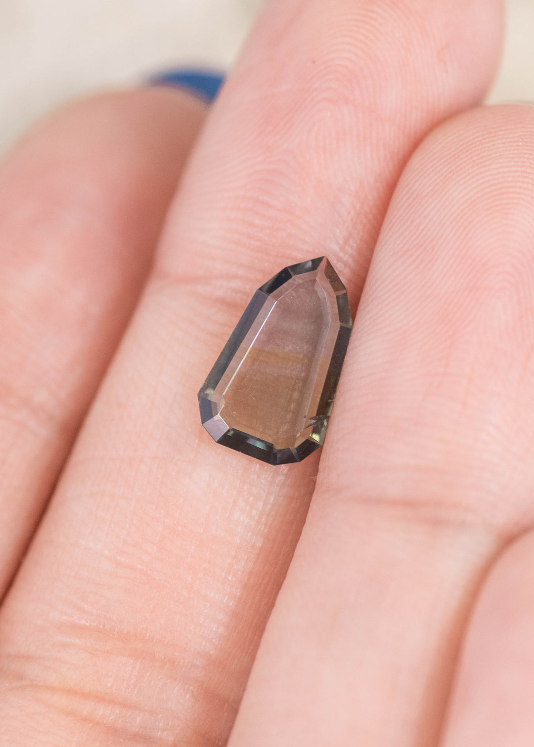 1.42 carat yellowish teal green blue Tanzanite shield portrait cut resting on finger, thin precision cut gemstone from Tanzania highlighting geometric edges, unique faceting and multicolor brilliance for bespoke jewelry