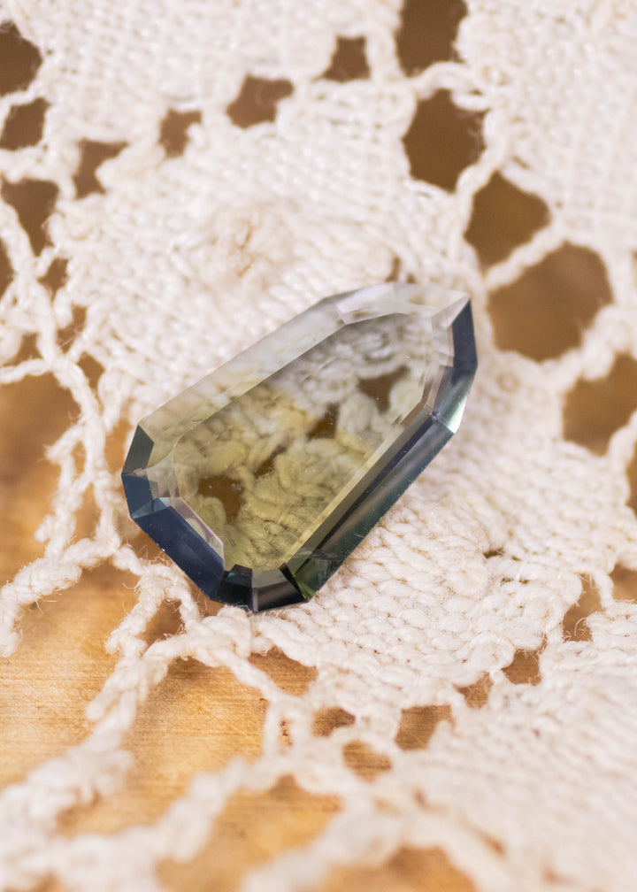 1.42 carat yellowish teal green blue Tanzanite shield portrait cut displayed on lace surface, precision faceted gemstone from Merelani Hills Tanzania showing thin profile, step facets and unique designer cut for custom jewelry