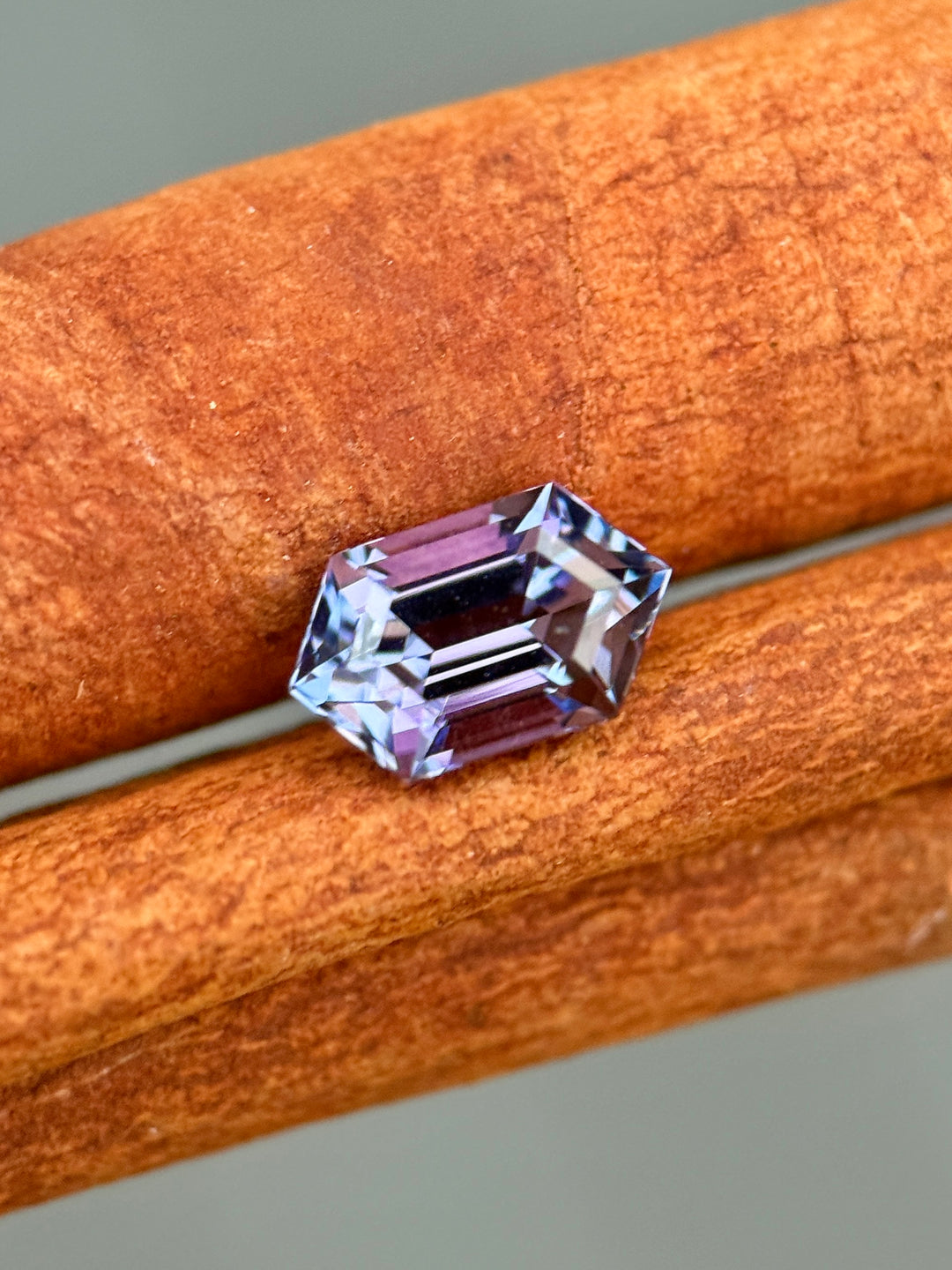 1.43-carat tanzanite gemstone in a step cut hexagon shape showing blue, green, pink, and purple mermaid colors, displayed on a cinnamon-colored textured background to highlight its untreated clarity and brilliance from Merelani Hills, Tanzania.