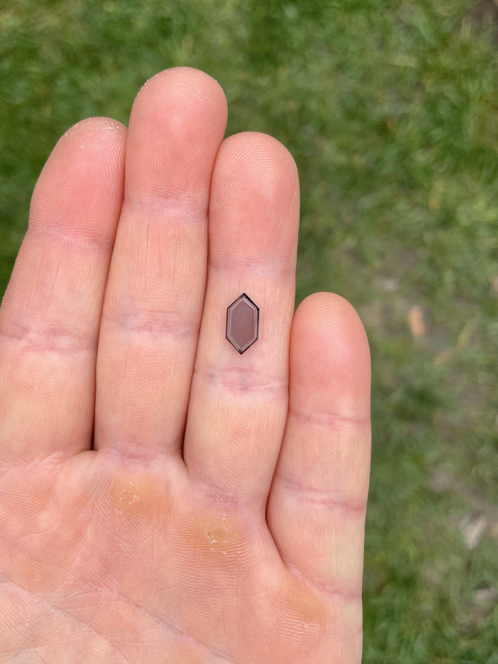 1.43 carat hexagonal step cut spinel with blue-gray tones held between fingers on green grass background