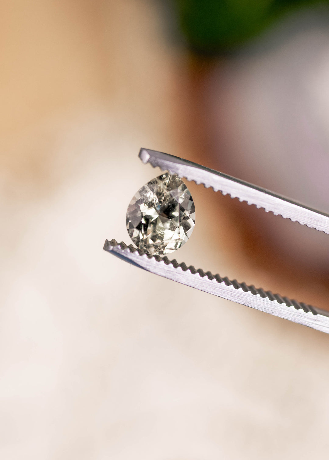 1.45 carat light teal Montana sapphire held in gem tweezers, highlighting the modified pear cut, sharp facet junctions, and natural untreated brilliance.