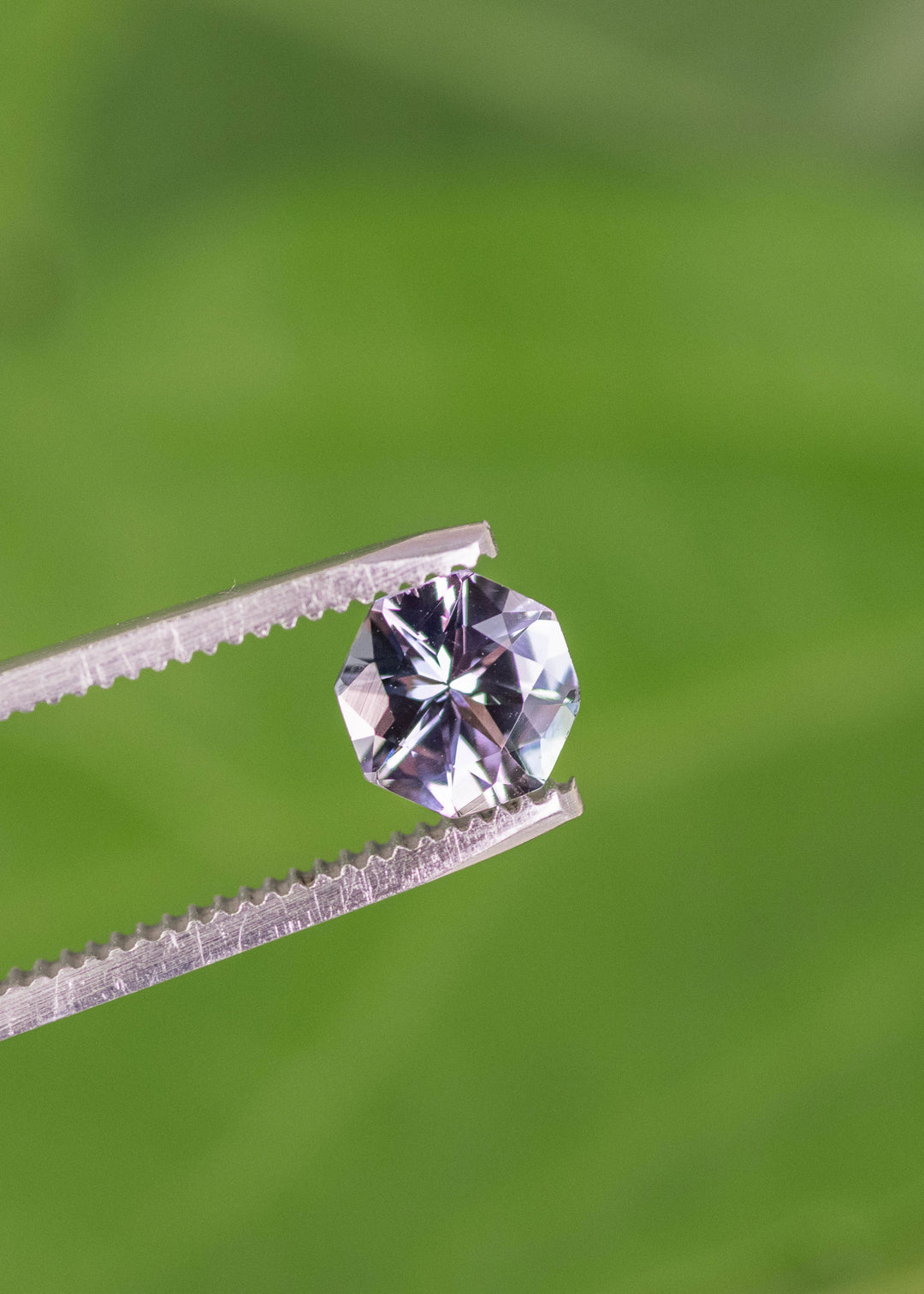 1.49 carat teal green lavender purple Tanzanite mix brilliant octagon held in tweezers, Merelani Hills Arusha Tanzania gemstone displaying sharp facet reflections, sparkle and color shift for fine jewelry design