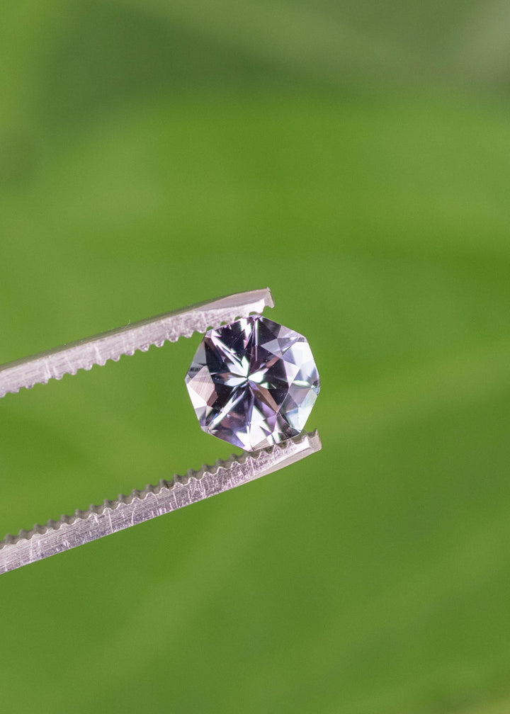 1.49 carat teal green lavender purple Tanzanite mix brilliant octagon held in tweezers, Merelani Hills Arusha Tanzania gemstone displaying sharp facet reflections, sparkle and color shift for fine jewelry design