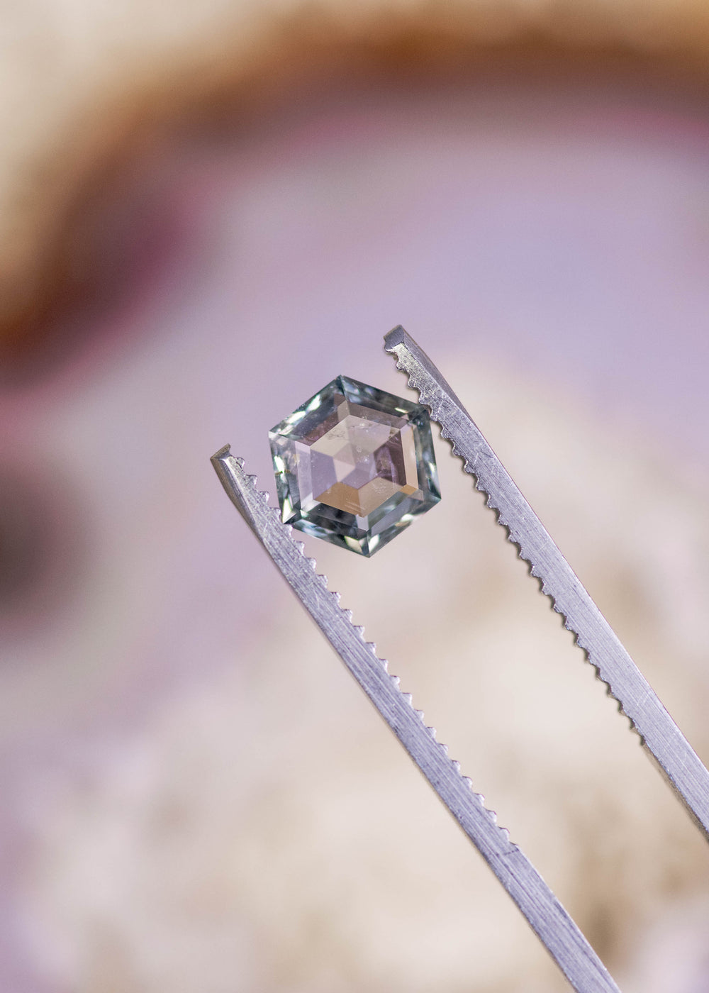 1.49ct Montana sapphire held in gem tweezers showing hexagon step cut faceting, natural green violet teal color shift, unheated gemstone from El Dorado Bar Deposit with crisp geometric edges.