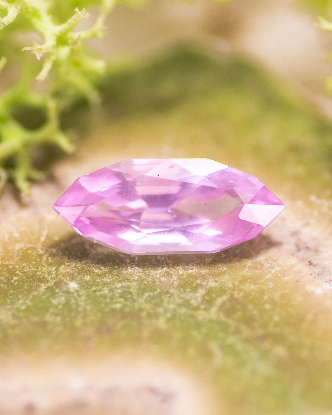 1.50 carat bubblegum pink sapphire resting on a mossy green surface, highlighting vivid saturation and brilliance of the precision marquise mixed cut, untreated sapphire from Sakaraha, Madagascar.