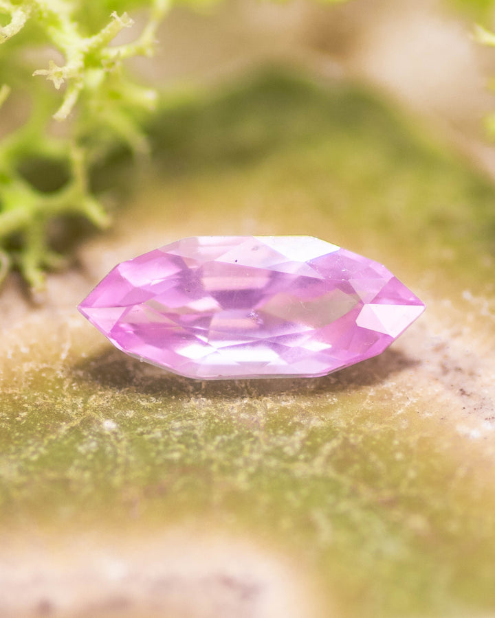 1.50 carat bubblegum pink sapphire resting on a mossy green surface, highlighting vivid saturation and brilliance of the precision marquise mixed cut, untreated sapphire from Sakaraha, Madagascar.