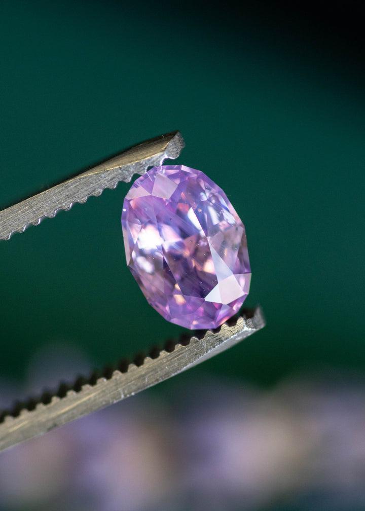Unheated 1.50 carat violet pink sapphire precision oval mix cut held in tweezers
