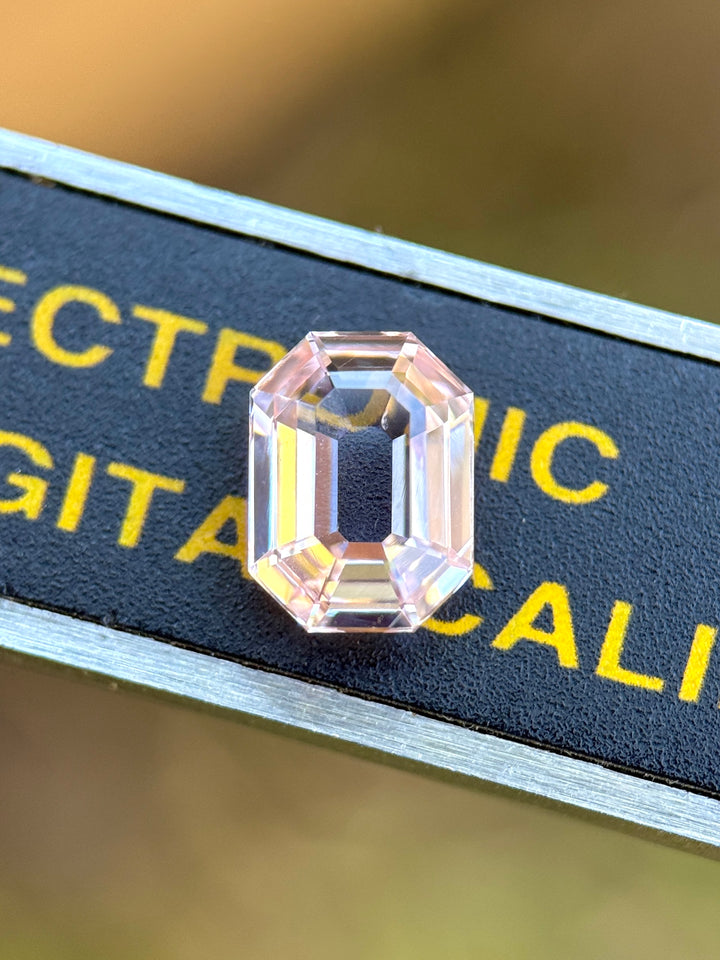 1.50 carat blush pink sapphire placed on digital caliper for scale, displaying symmetry, radiant sparkle, and the elegant proportions of the precision antique emerald cut, untreated gem from Sakaraha, Madagascar.
