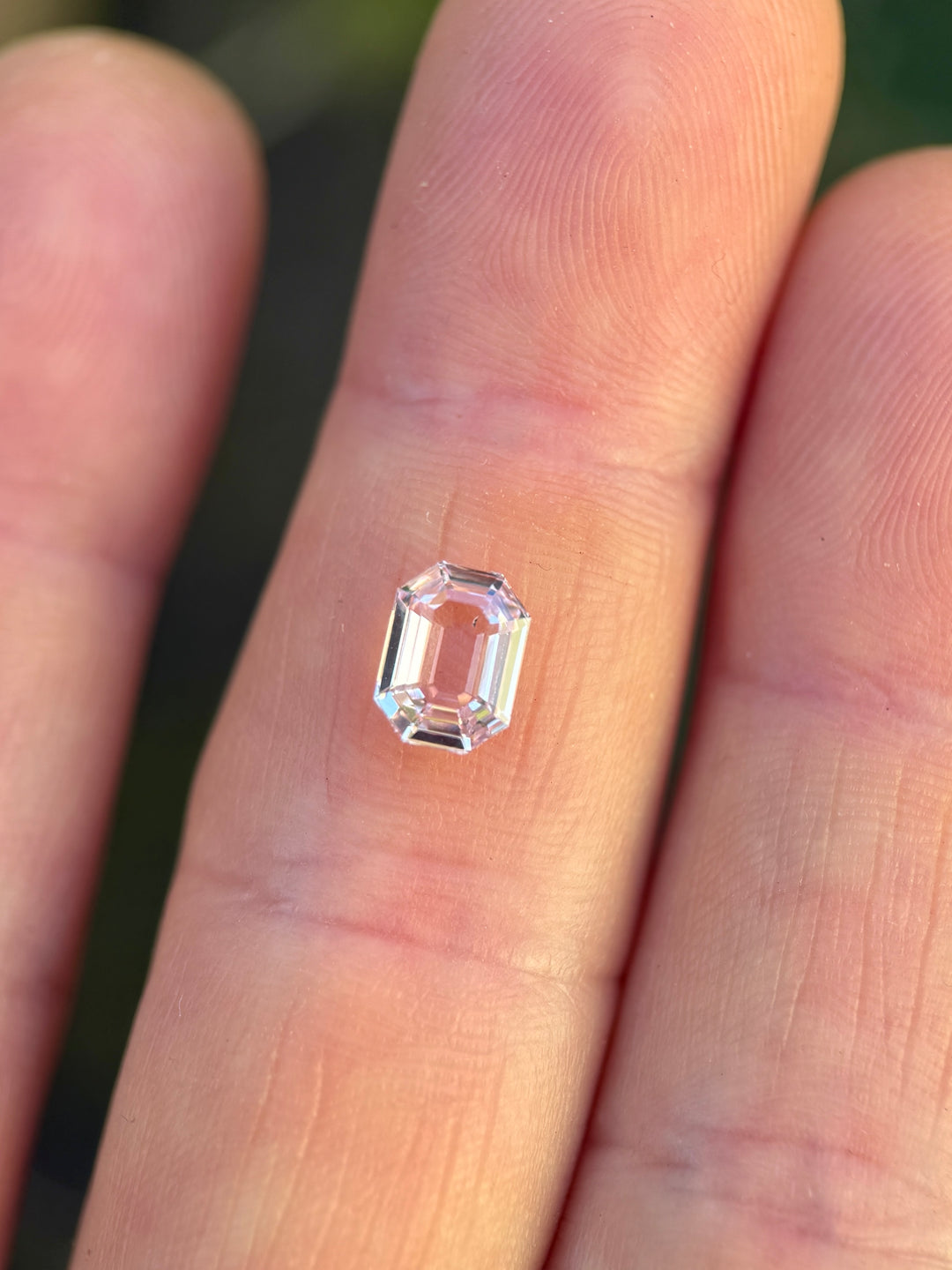 1.50 carat blush pink sapphire resting on fingertips in natural sunlight, showing exceptional clarity, step faceting, and antique emerald cut brilliance of the untreated gemstone from Sakaraha, Madagascar.