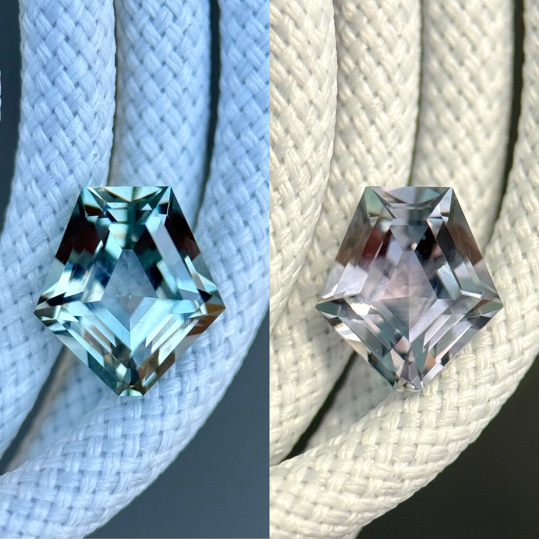 Montana sapphire resting on textured white background, transitioning from cool teal to soft purple hues