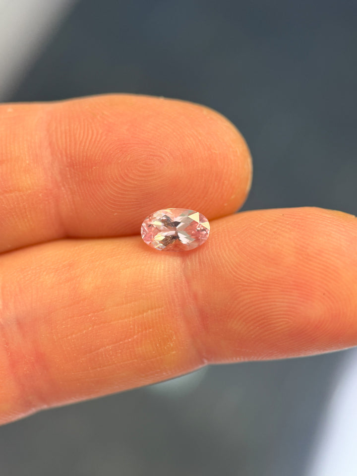 1.50 carat salmon pink sapphire held between fingers showing oval modified brilliant cut and high clarity