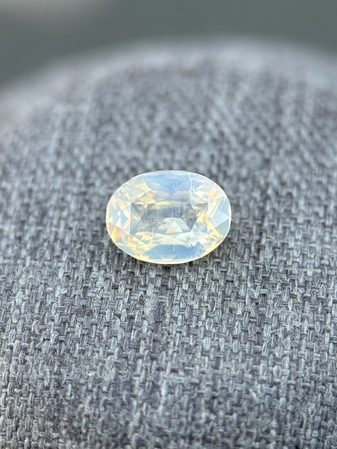 1.50ct oval brilliant sapphire on textured fabric, glowing with silvery opalescence and subtle peach and blue coloring