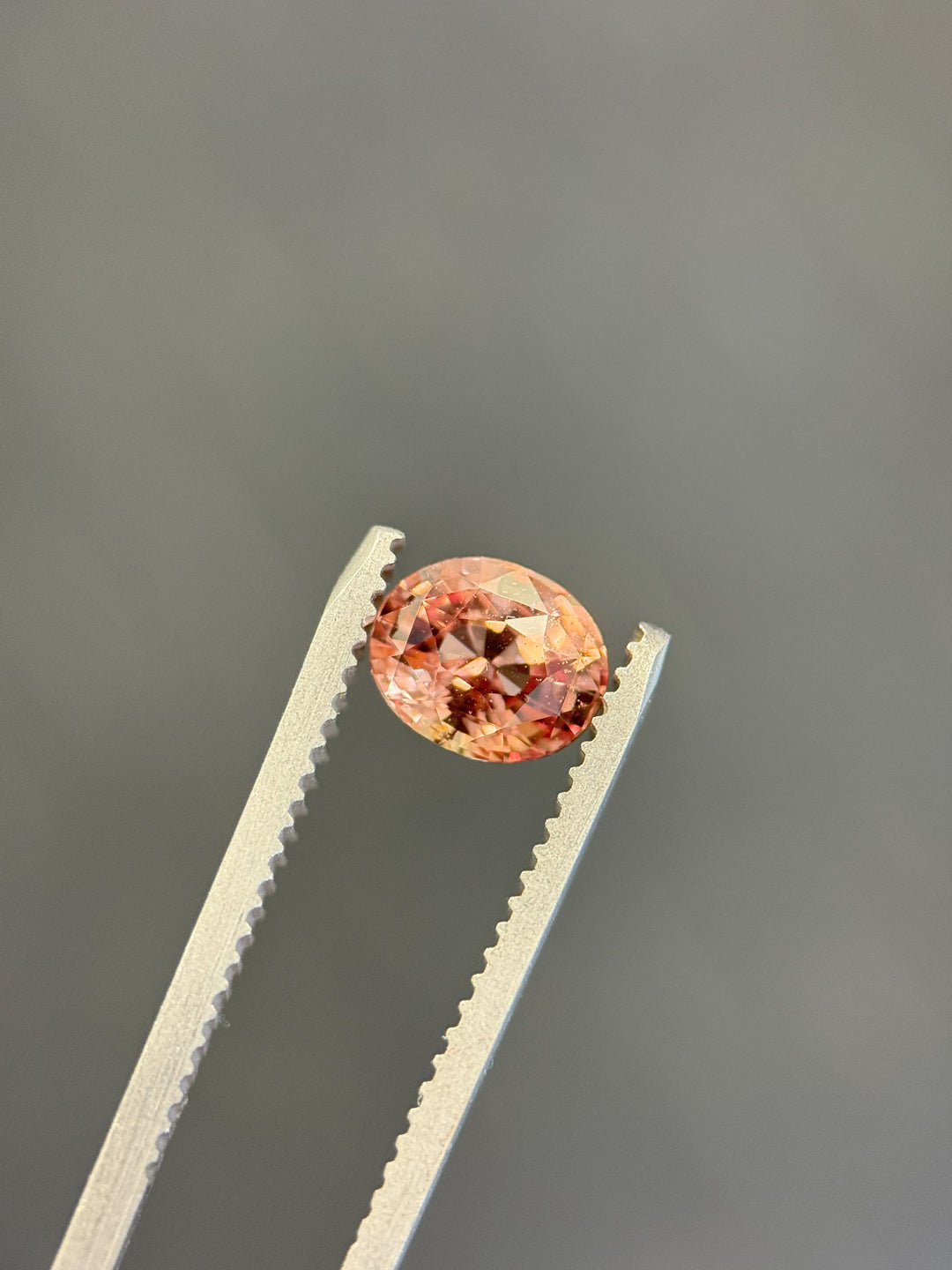 1.51-carat untreated peach-pink oval sapphire held in tweezers, showcasing brilliant mix cut from Sakaraha, Madagascar