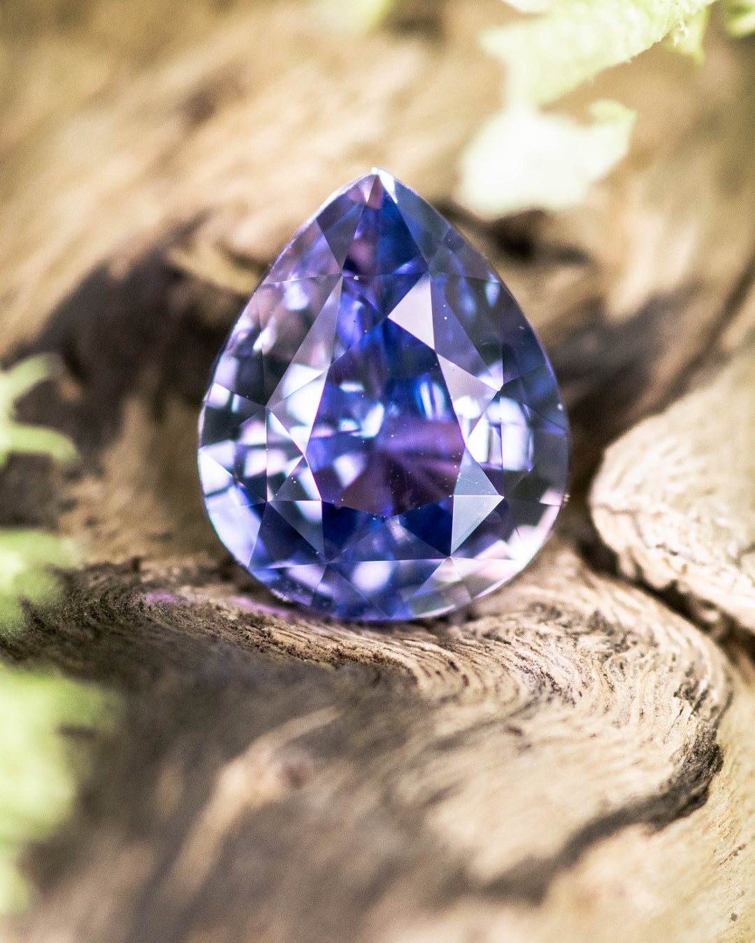 1.51 carat violet purple pink sapphire resting on natural wood, showcasing its vivid sparkle and precise pear brilliant cut, untreated gemstone from Sakaraha, Madagascar.